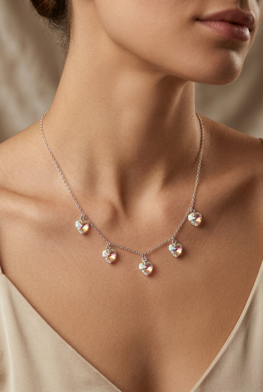A delicate silver chain necklace with five small iridescent heart charms, displayed on a woman.