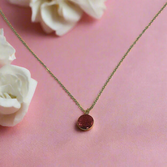 Ruby Crimson Shimmer Charm Necklace displayed on a pink background with white flowers.