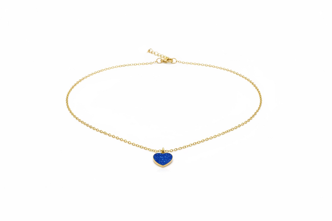 A delicate gold chain necklace with a small, textured royal blue heart-shaped pendant, displayed on a light wood grain surface.