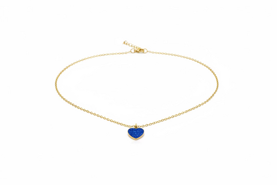 A delicate gold chain necklace with a small, textured royal blue heart-shaped pendant, displayed on a light wood grain surface.