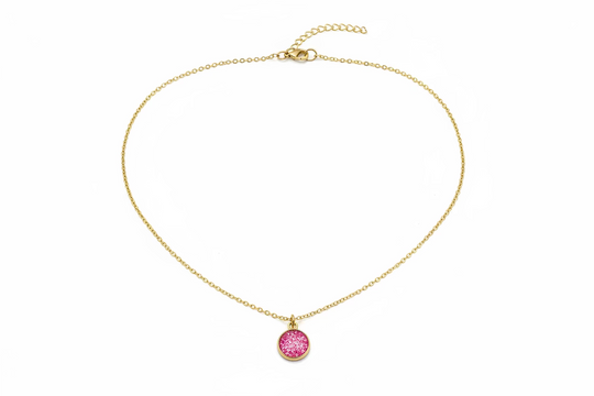 A delicate gold chain necklace with a small, round, dark red disc pendant, displayed on a light wood grain surface.