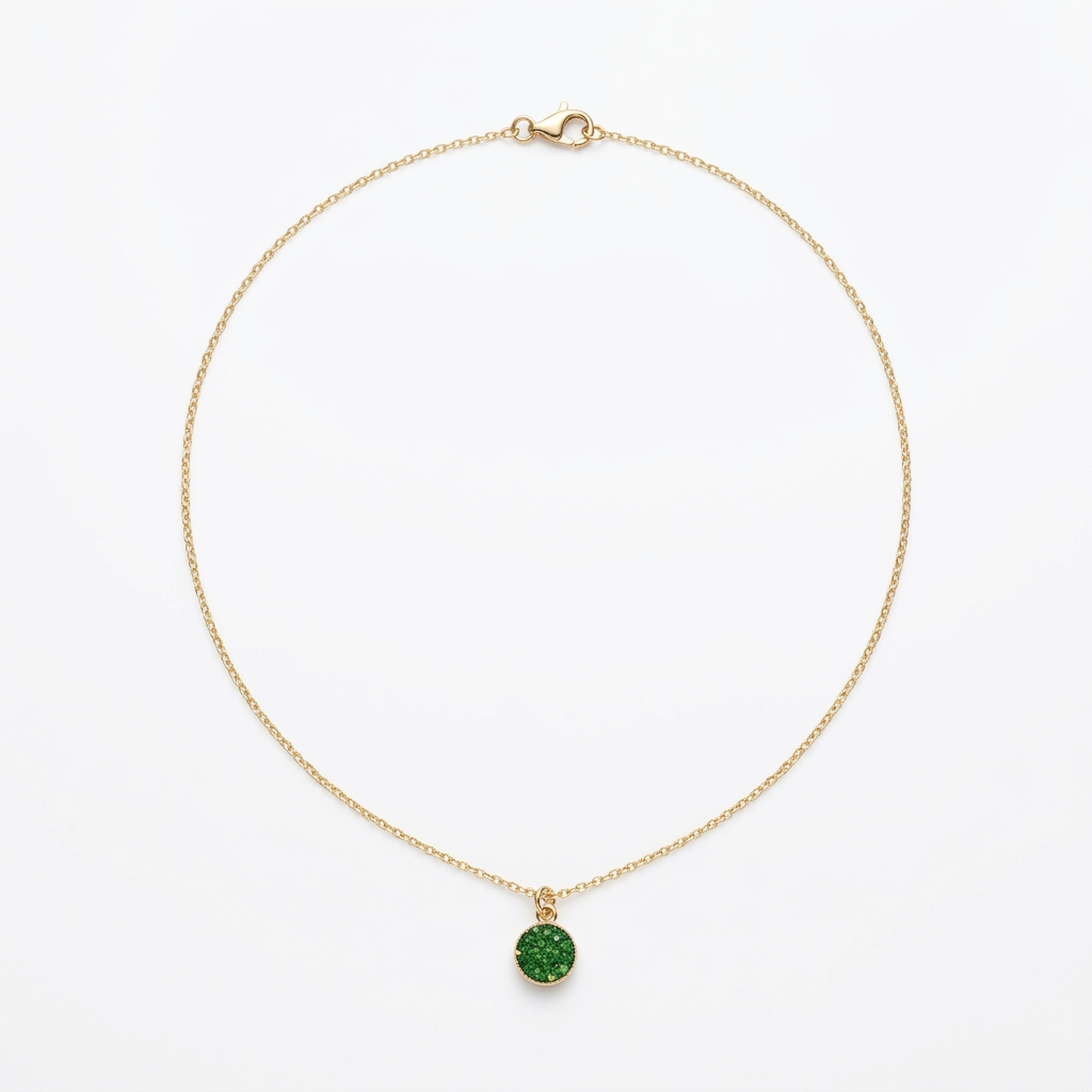 A delicate gold chain necklace with a small round green gemstone pendant, displayed on a textured gray surface with natural light casting shadows.