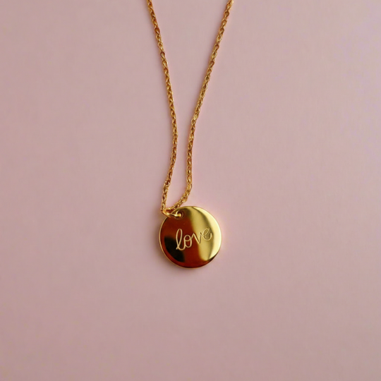 Gold Hand Stamped Love Necklace, our delicate gold disk necklace features a hand stamped "Love" message in simple script. Its minimalist design and 14K gold filled chain add a sweet, subtle touch making it a treasure to adore.